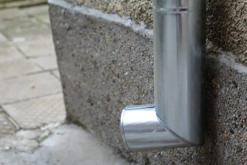 Close-up of a metal downpipe and its shoe against a rendered block wall
