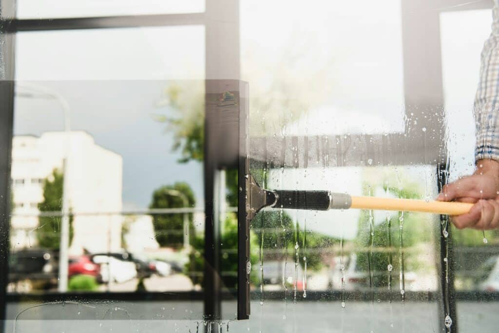 cropped shot of cleaner washing window with detergent and water