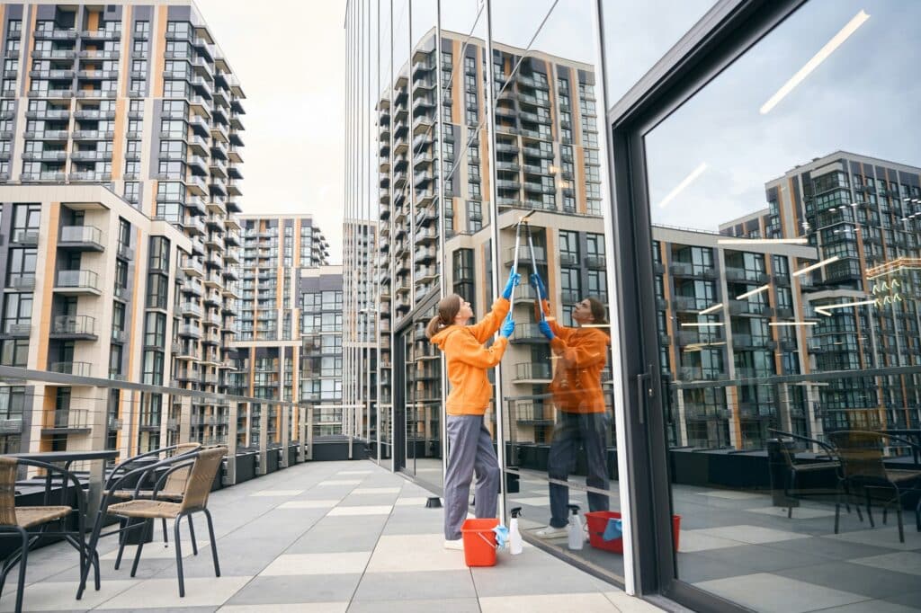 Pretty cleaning company employee in a warm sweatshirt washes mirrored windows